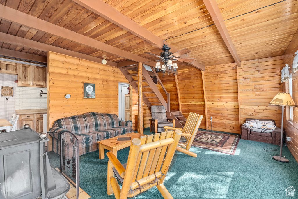 Carpeted living room featuring beam ceiling, wooden walls, stairs, a ceiling fan, and wood ceiling