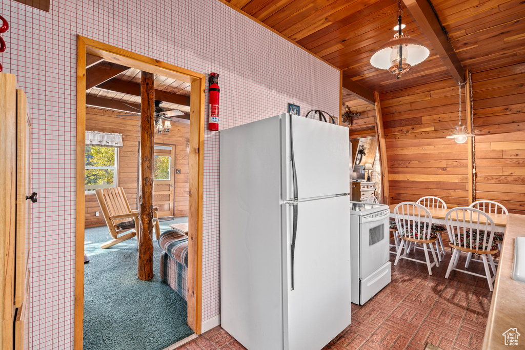 Kitchen with white appliances, wooden ceiling, wood walls, brick patterned flooring, and a ceiling fan
