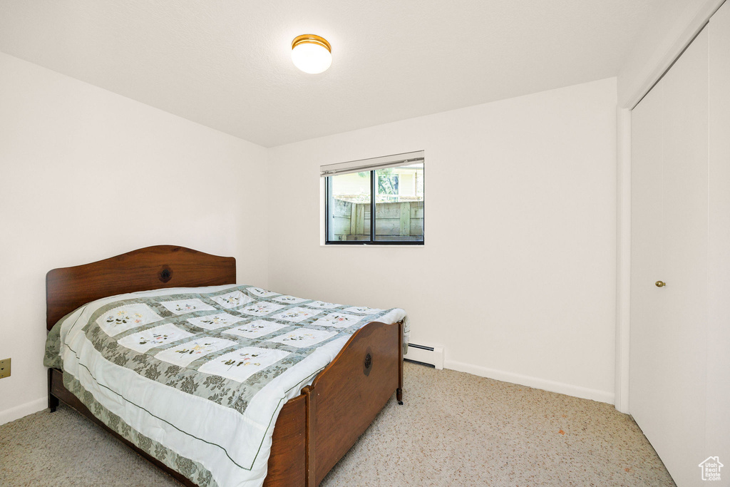 Bedroom with a baseboard heating unit, carpet flooring, baseboards, and a closet