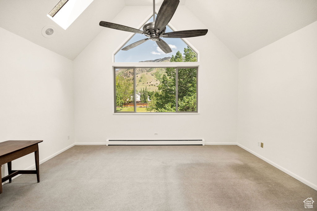 Carpeted spare room featuring baseboard heating, a skylight, baseboards, a ceiling fan, and high vaulted ceiling