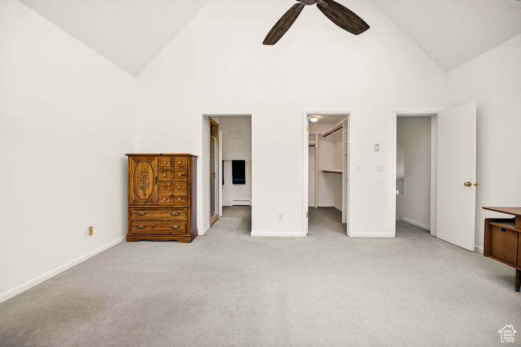 Unfurnished bedroom with light carpet, baseboards, high vaulted ceiling, a spacious closet, and a baseboard heating unit