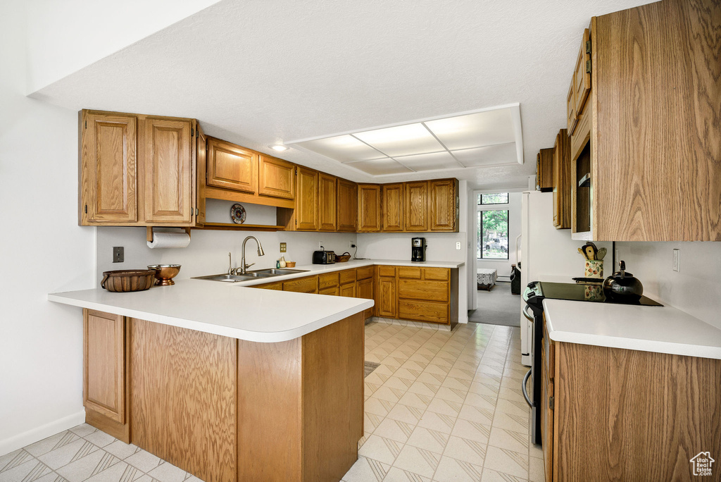 Kitchen featuring a sink, a peninsula, light countertops, and brown cabinetry