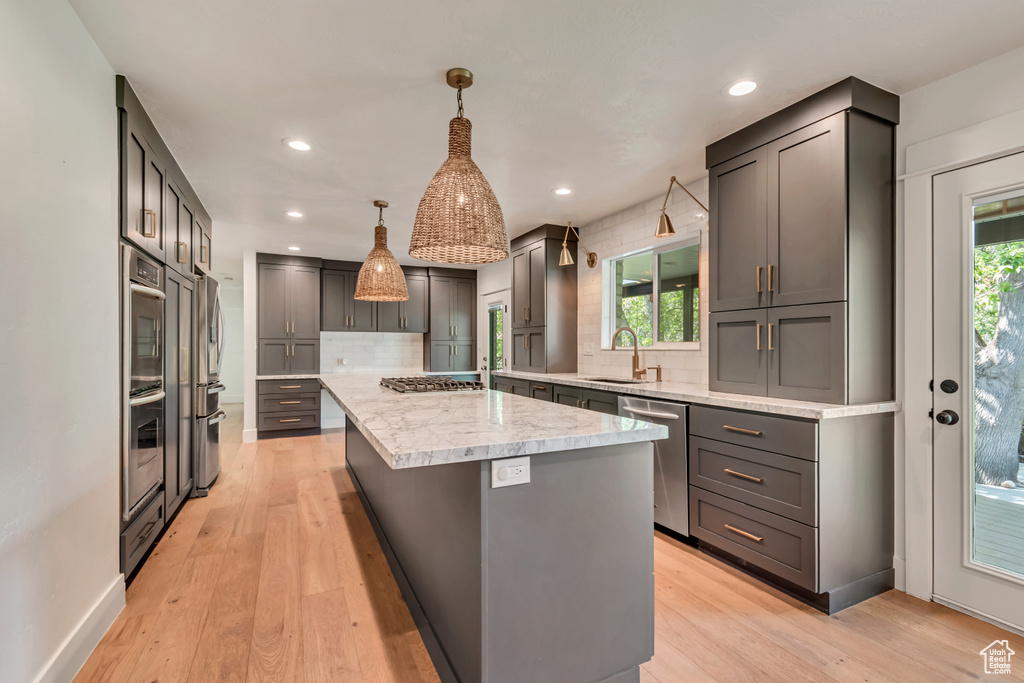 Kitchen featuring stainless steel appliances, a kitchen island, decorative backsplash, light wood-style floors, and recessed lighting