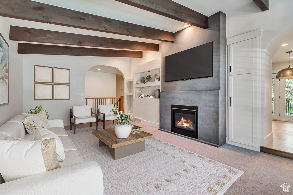 Living room with arched walkways, beamed ceiling, a fireplace, carpet floors, and baseboards