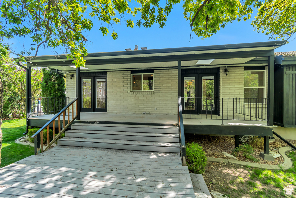 Rear view of house featuring brick siding, covered porch, and french doors
