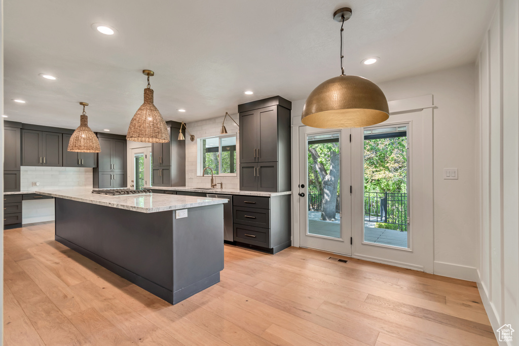 Kitchen with plenty of natural light, backsplash, light stone countertops, recessed lighting, and light wood-style floors