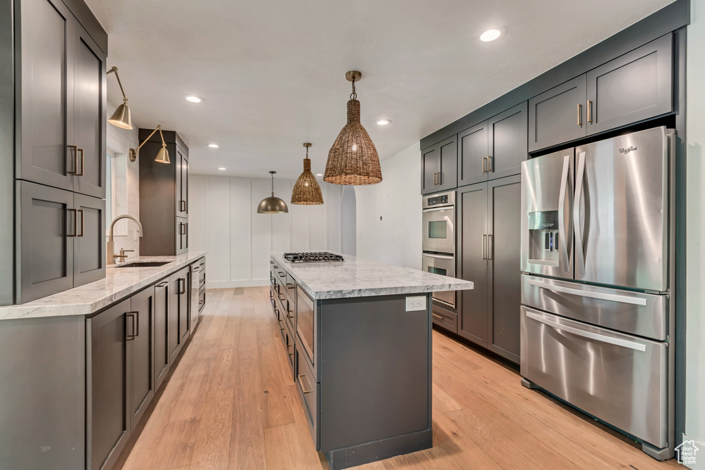 Kitchen with appliances with stainless steel finishes, a sink, a center island, light stone countertops, and light wood finished floors