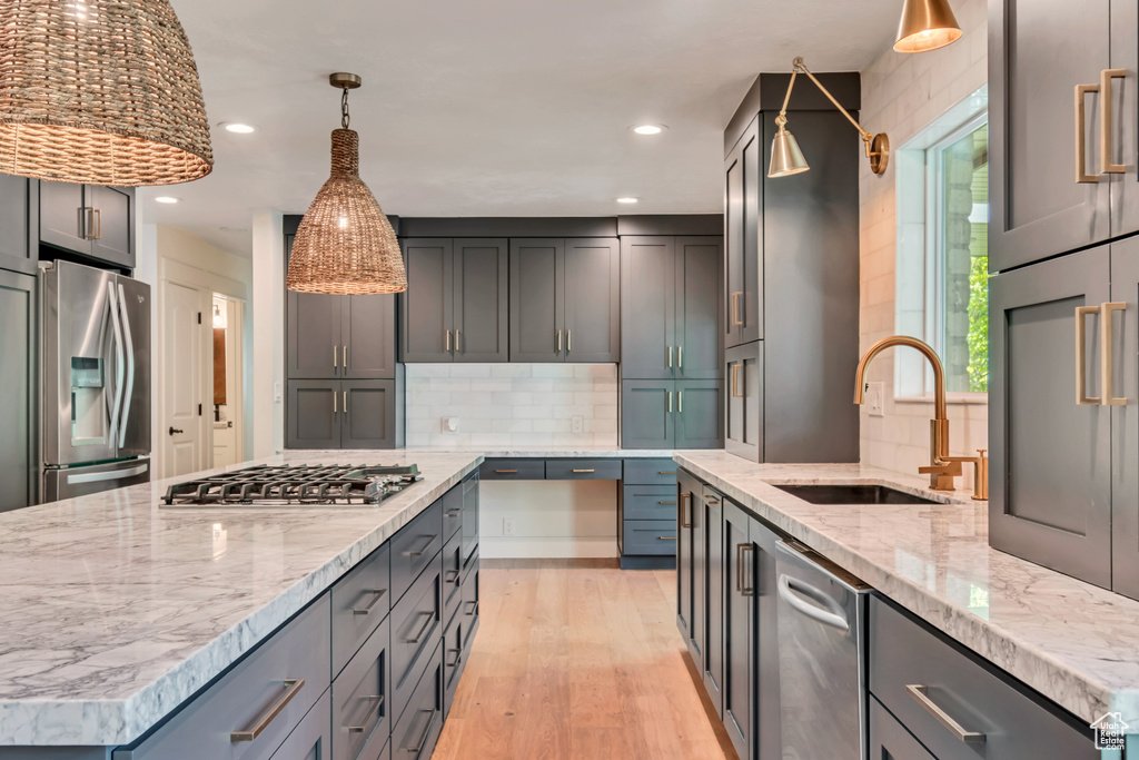 Kitchen with appliances with stainless steel finishes, a sink, light stone counters, light wood-type flooring, and recessed lighting