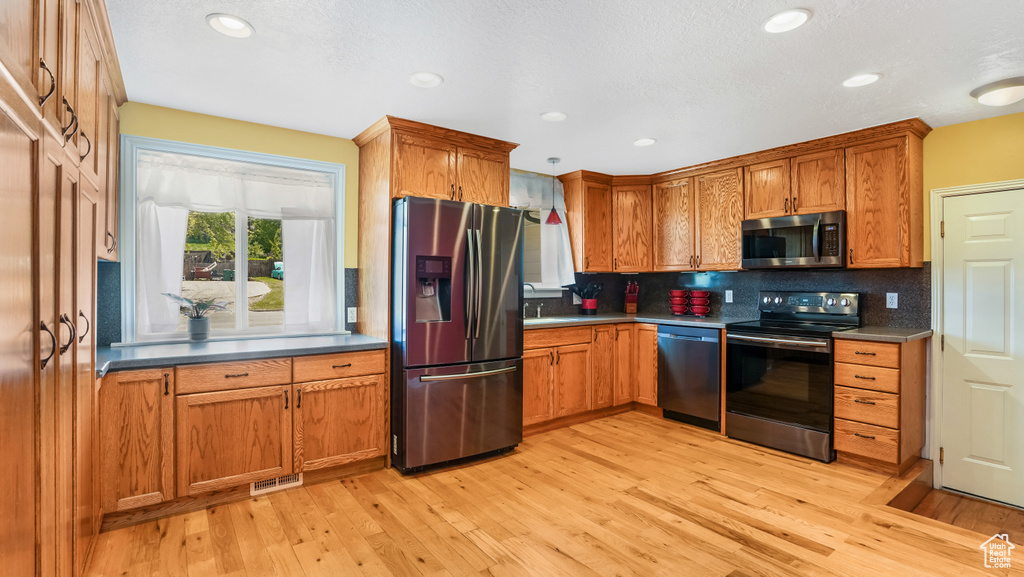Kitchen with stainless steel appliances, light wood-type flooring, backsplash, brown cabinets, and recessed lighting