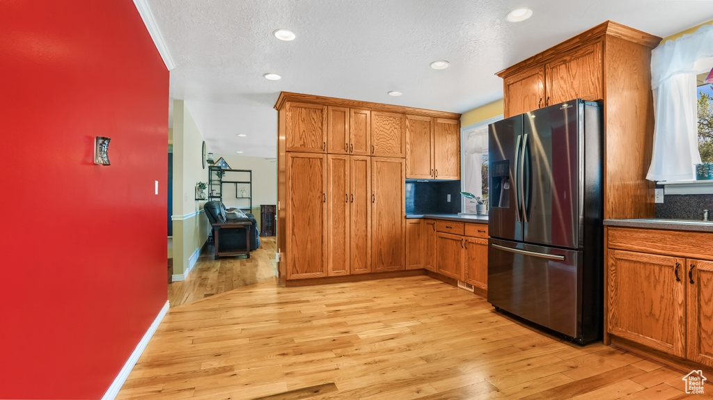 Kitchen featuring stainless steel fridge with ice dispenser, brown cabinetry, light wood finished floors, recessed lighting, and baseboards