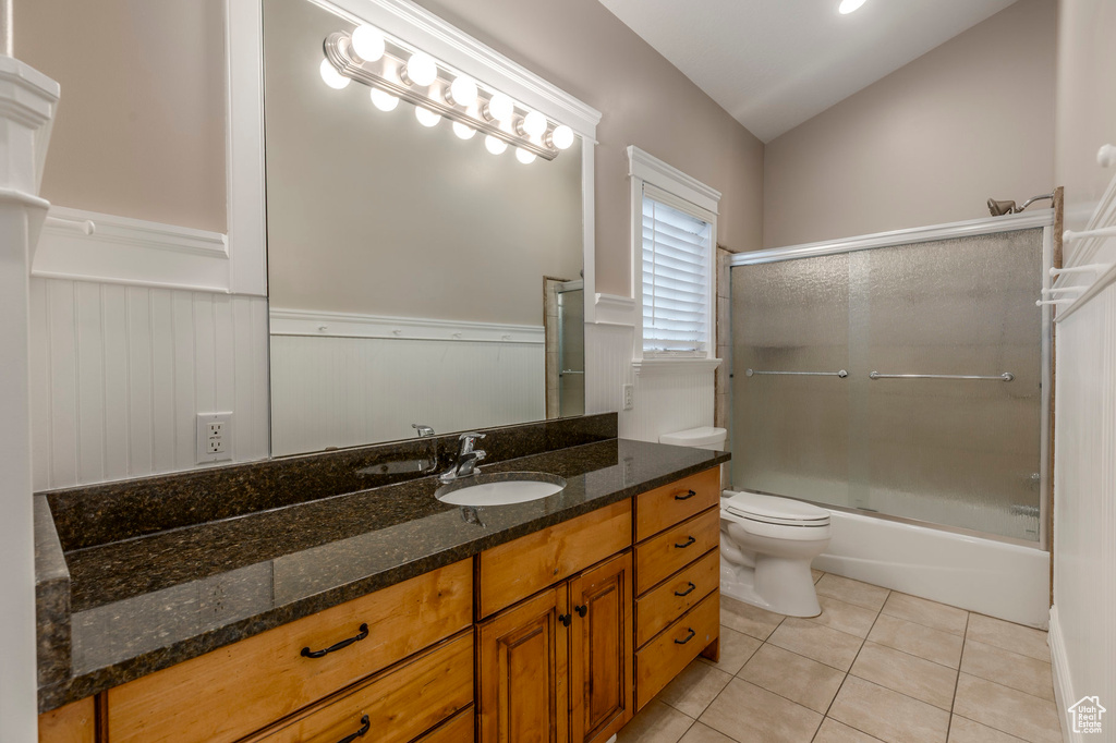 Full bathroom with a wainscoted wall, tile patterned flooring, vanity, toilet, and shower / bath combination with glass door