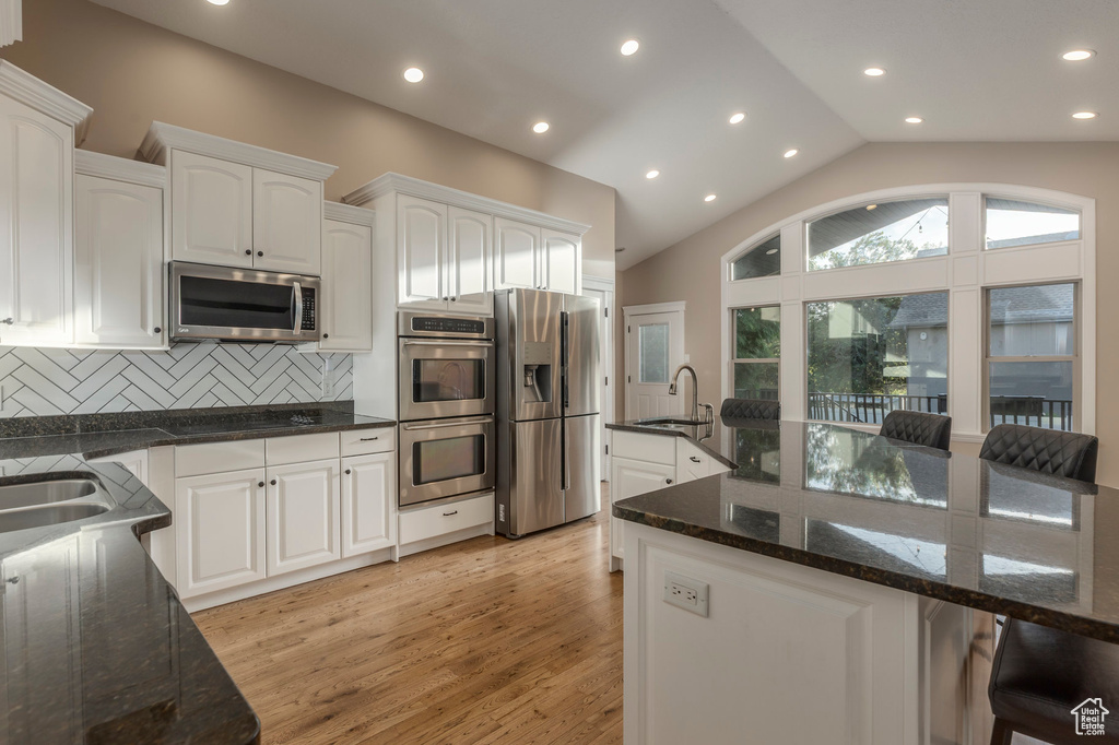 Kitchen with appliances with stainless steel finishes, a sink, white cabinetry, decorative backsplash, and vaulted ceiling