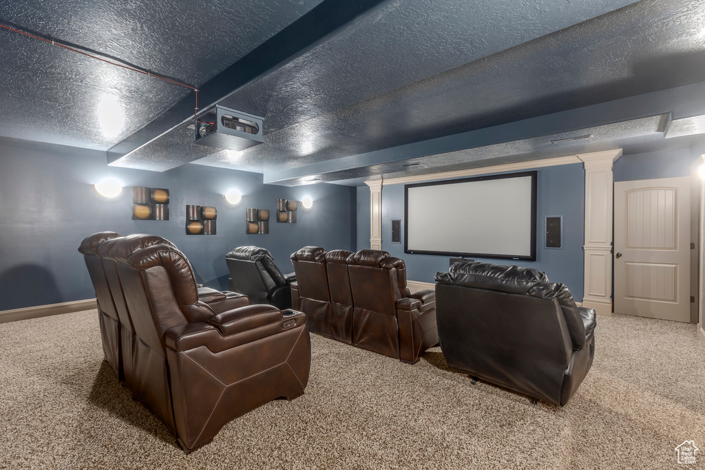 Home theater room with carpet flooring, decorative columns, baseboards, and a textured ceiling
