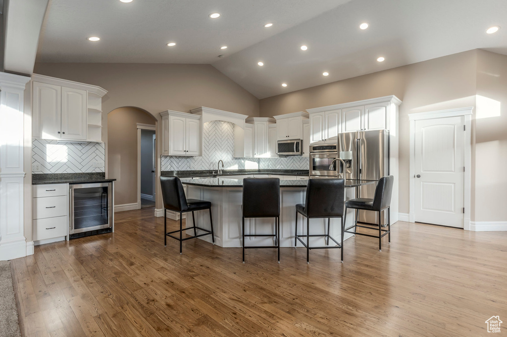 Kitchen featuring wine cooler, stainless steel appliances, open shelves, lofted ceiling, and white cabinets