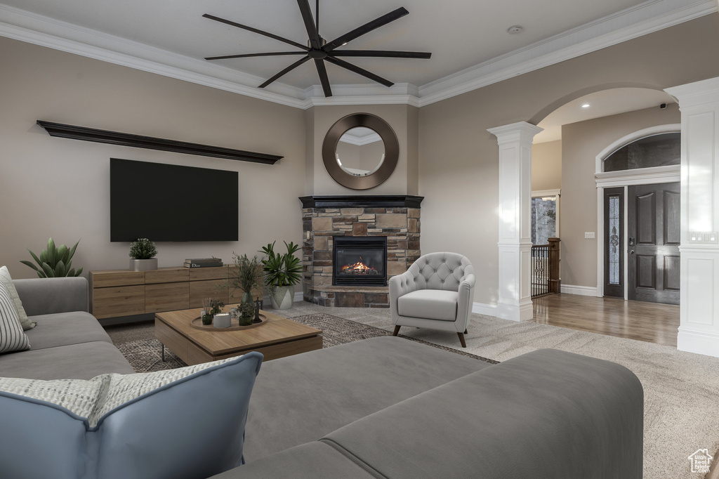 Living room featuring ornate columns, ornamental molding, ceiling fan, a stone fireplace, and wood finished floors