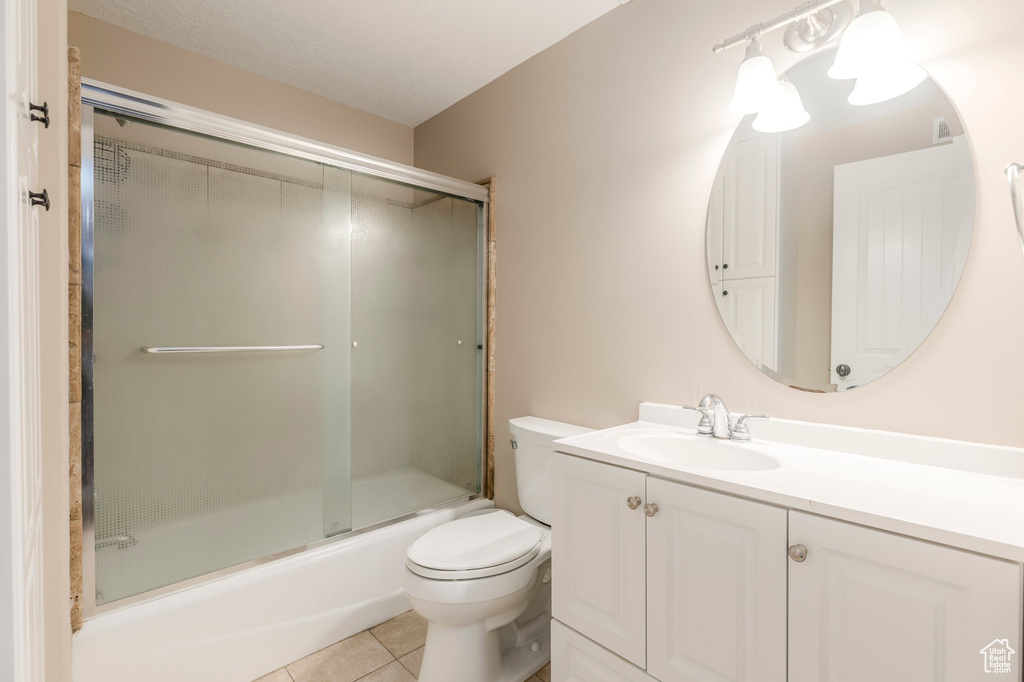 Bathroom featuring toilet, tile patterned flooring, vanity, and enclosed tub / shower combo