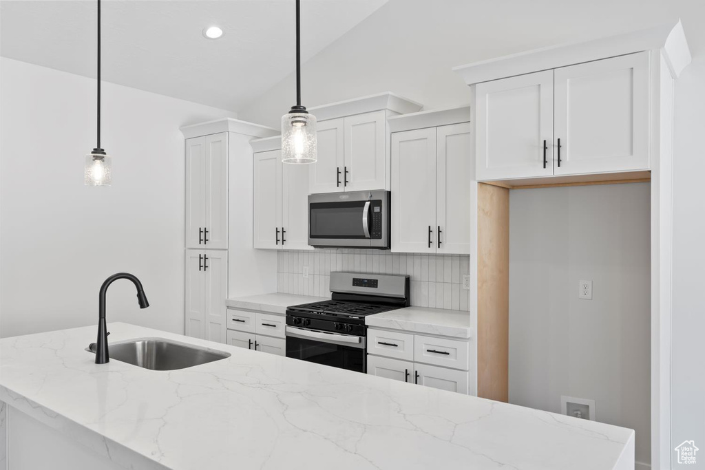 Kitchen featuring stainless steel appliances, a sink, tasteful backsplash, white cabinetry, and light stone counters
