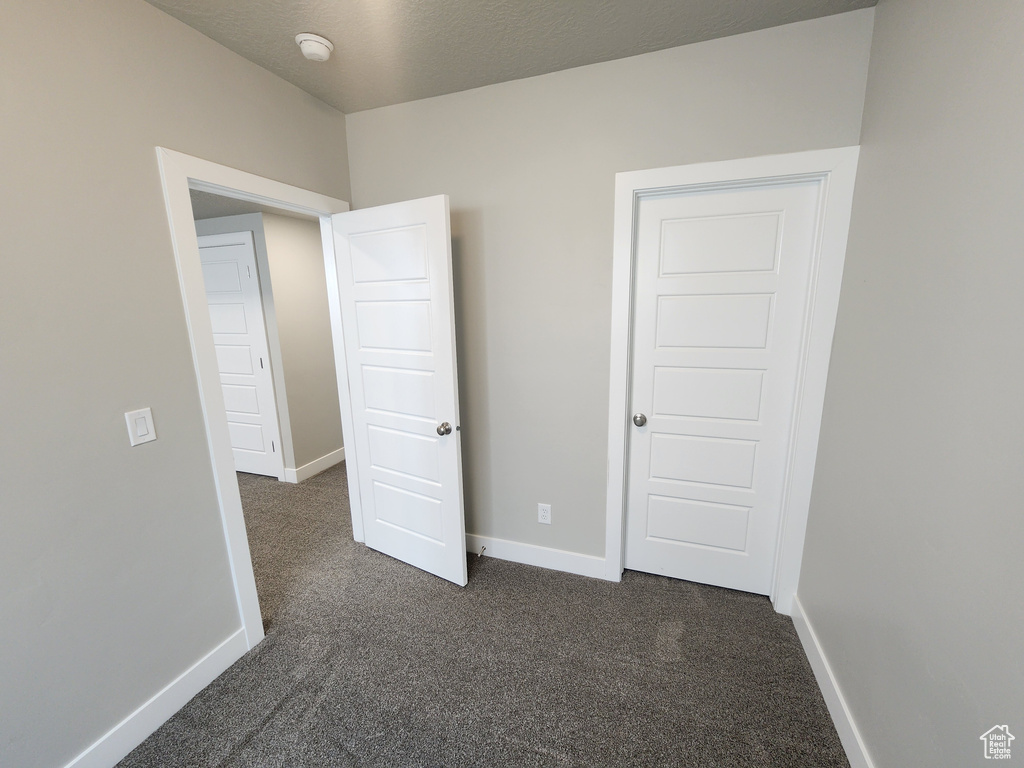 Unfurnished bedroom with dark carpet and baseboards