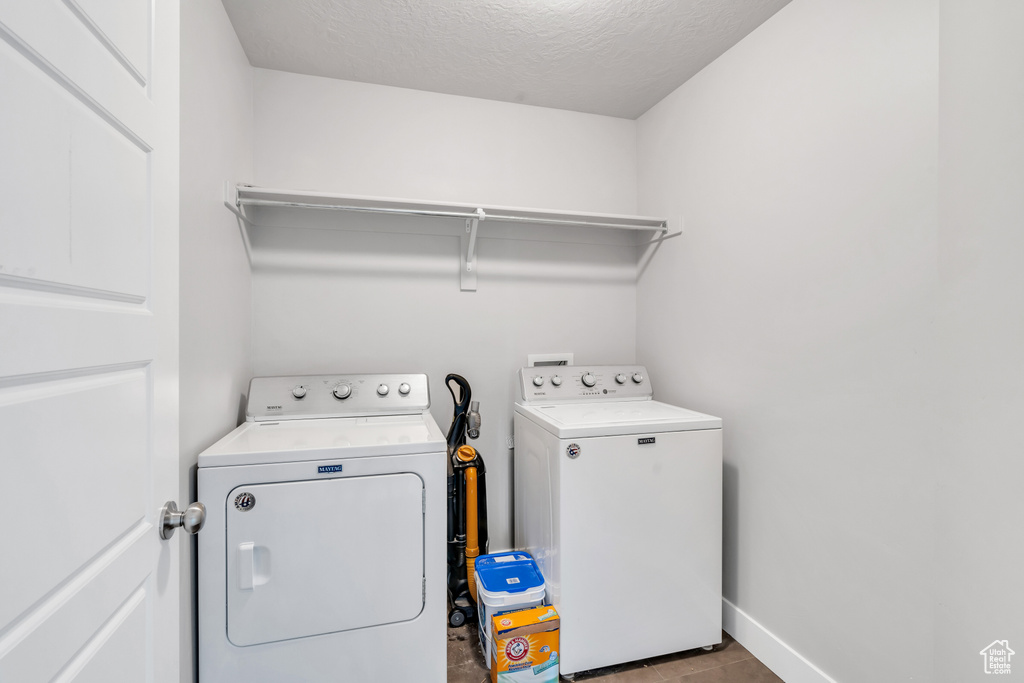 Laundry room with washer and clothes dryer, a textured ceiling, and baseboards