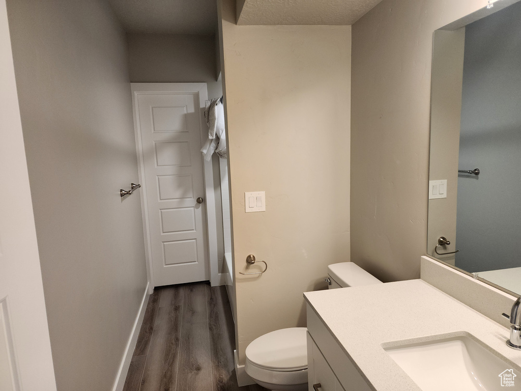 Full bath with toilet, wood finished floors, vanity, shower / tub combo with curtain, and baseboards