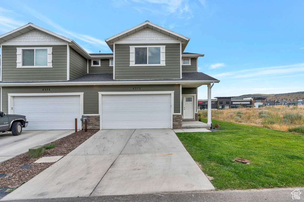 View of front of property featuring a front yard, concrete driveway, a garage, stone siding, and a shingled roof