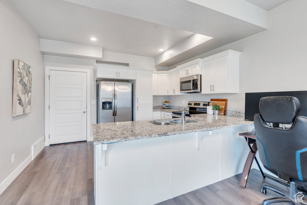 Kitchen with stainless steel appliances, a peninsula, white cabinets, light stone counters, and light wood-style floors