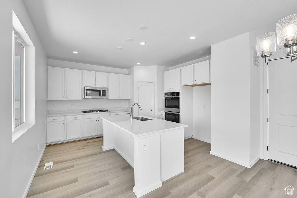 Kitchen with appliances with stainless steel finishes, a sink, recessed lighting, white cabinetry, and light wood-style floors