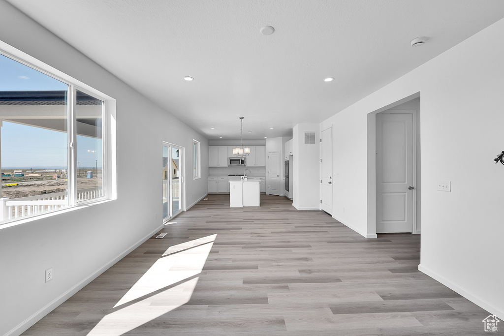 Unfurnished living room featuring recessed lighting, baseboards, light wood-style floors, a chandelier, and a sink