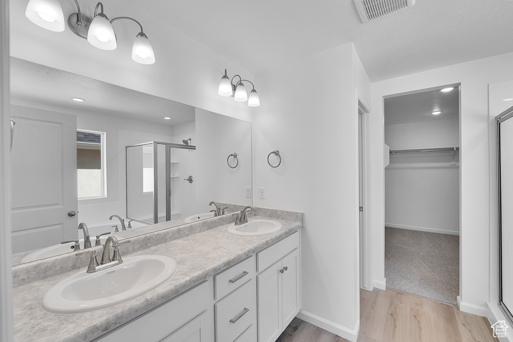 Bathroom featuring wood finished floors, a stall shower, double vanity, and a spacious closet