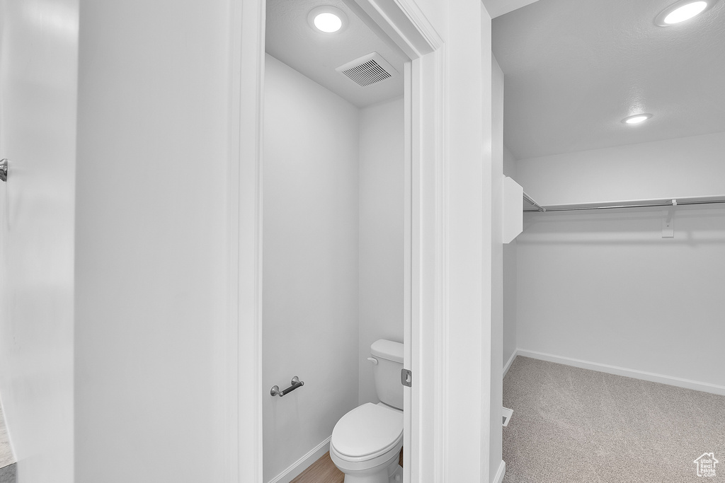 Bathroom with recessed lighting, toilet, baseboards, and a walk in closet