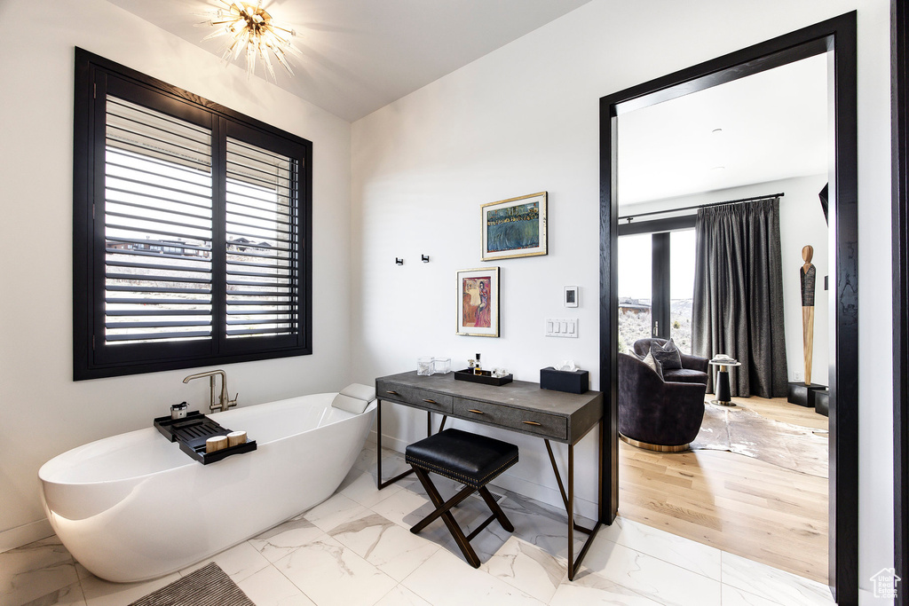 Full bath with marble look tiles, a freestanding bath, and baseboards