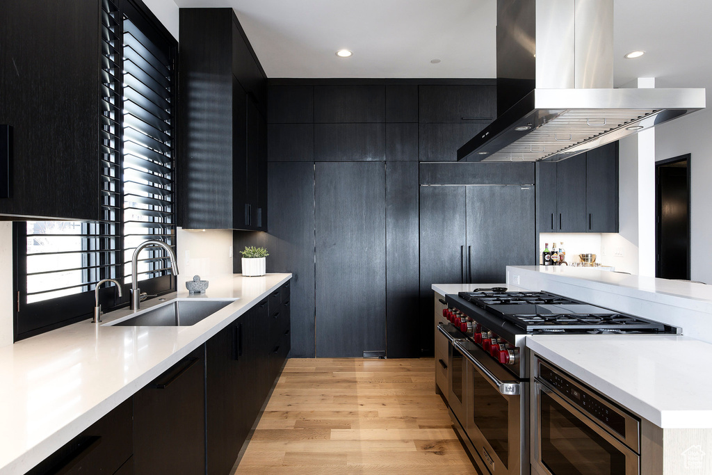 Kitchen featuring island exhaust hood, a sink, dark cabinetry, light wood-style flooring, and recessed lighting