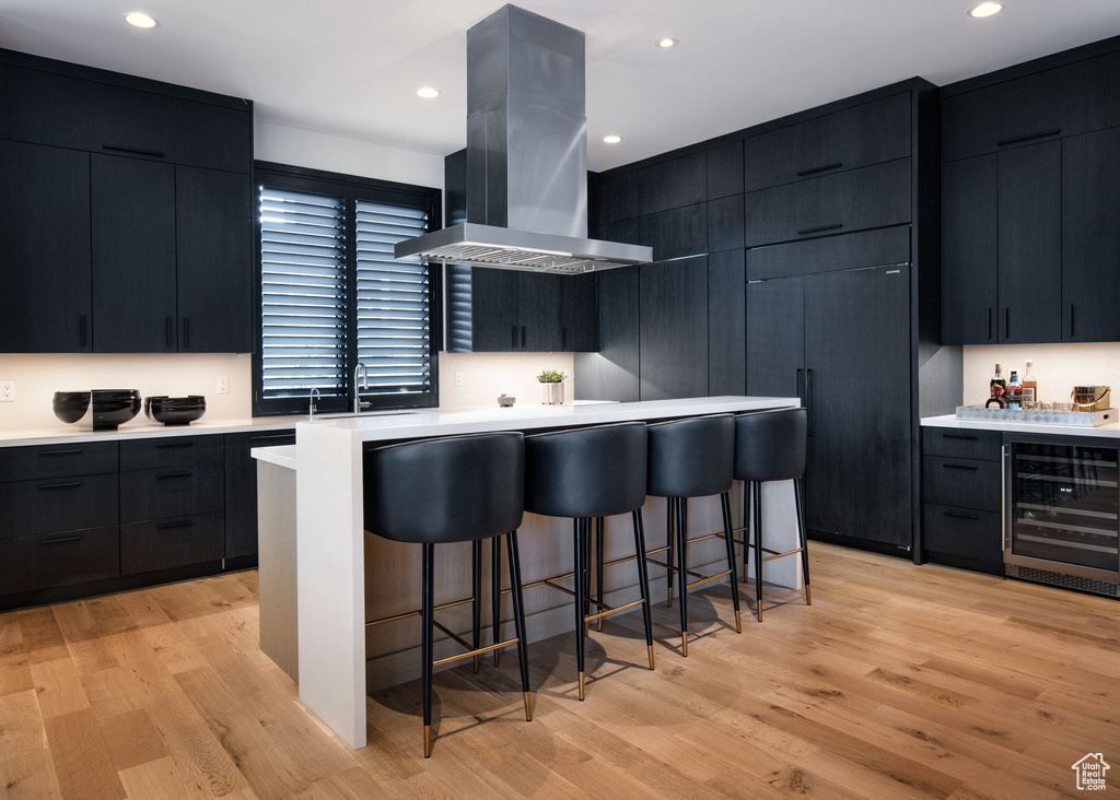 Kitchen featuring beverage cooler, island range hood, dark cabinetry, modern cabinets, and recessed lighting