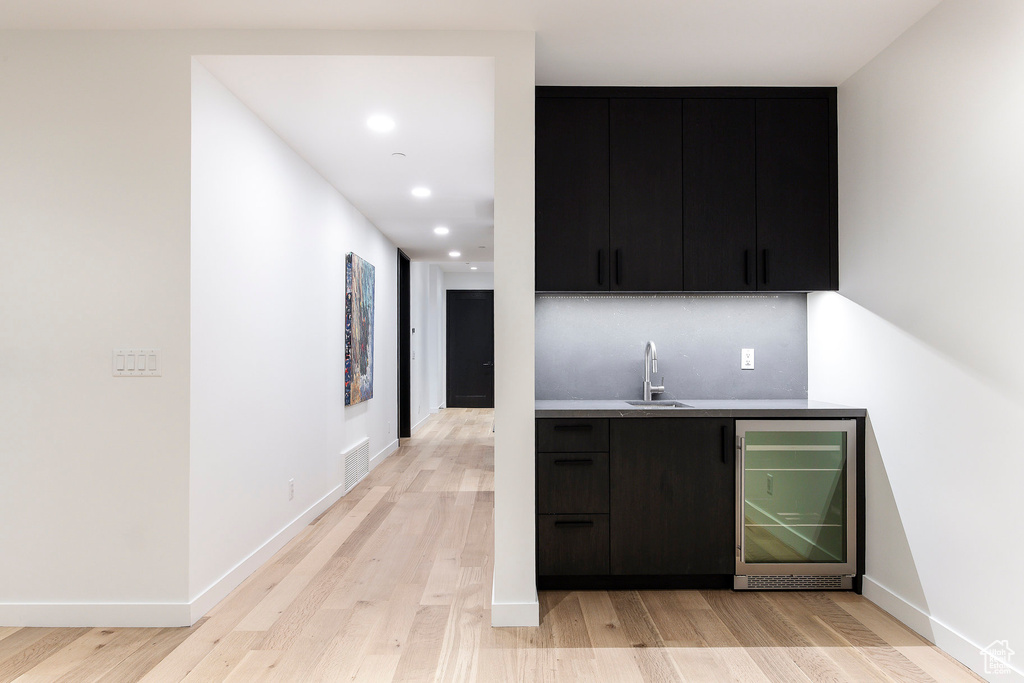 Indoor wet bar featuring beverage cooler, light wood-style floors, recessed lighting, and baseboards