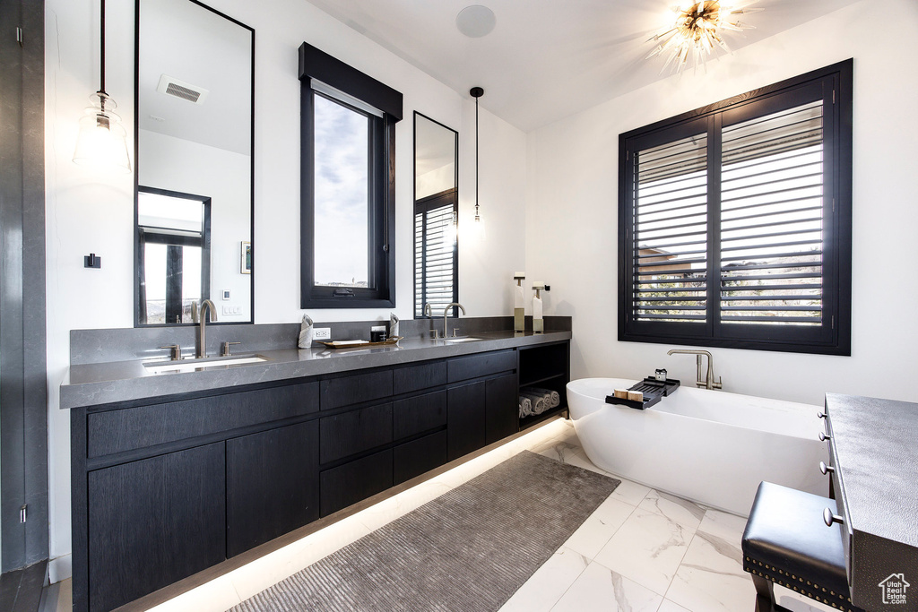 Bathroom featuring marble look tiles, healthy amount of natural light, a freestanding tub, and double vanity