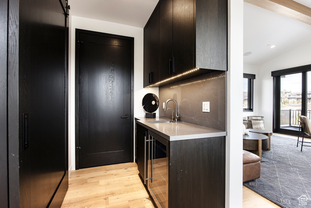 Kitchen with a sink, wine cooler, light countertops, light wood-style flooring, and vaulted ceiling