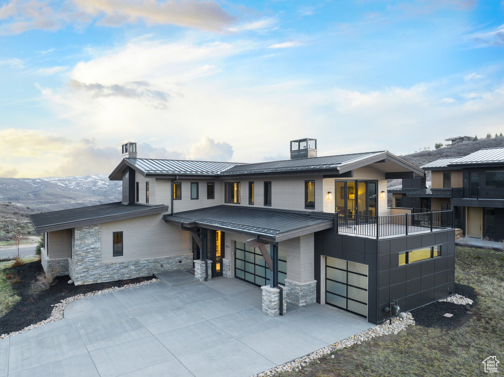 Contemporary house with a standing seam roof, a garage, stone siding, metal roof, and a balcony