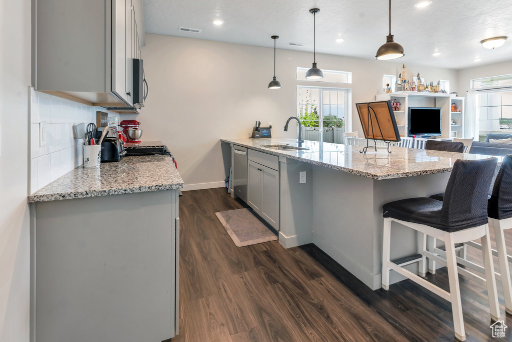 Kitchen featuring a sink, gray cabinets, appliances with stainless steel finishes, dark wood-style floors, and a breakfast bar