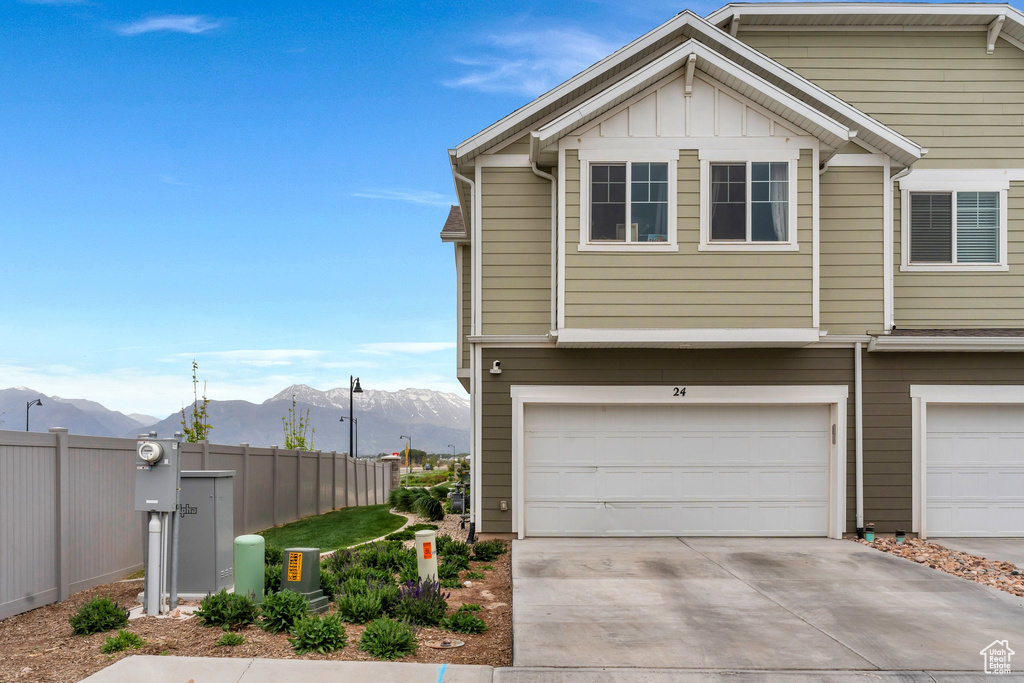 View of side of home featuring a mountain view, fence, driveway, a garage, and board and batten siding