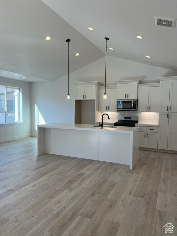 Kitchen featuring appliances with stainless steel finishes, a sink, lofted ceiling, recessed lighting, and light wood-type flooring