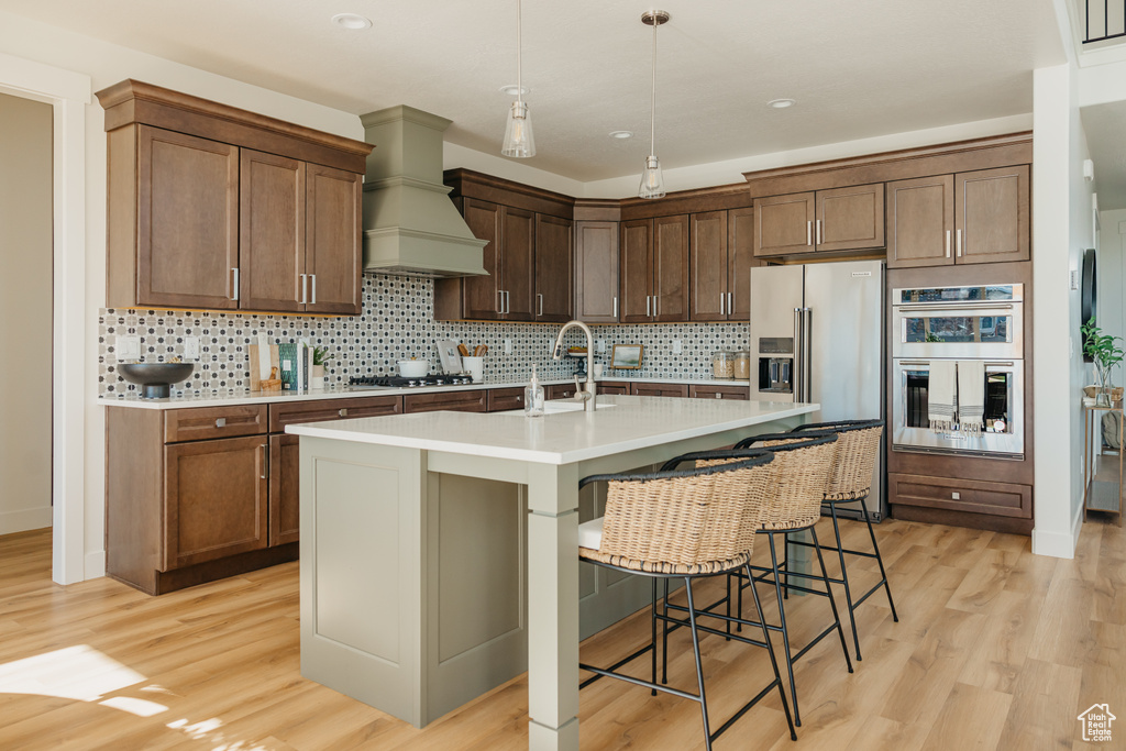 Kitchen with high end refrigerator, a sink, stainless steel double oven, light countertops, and light wood-style flooring