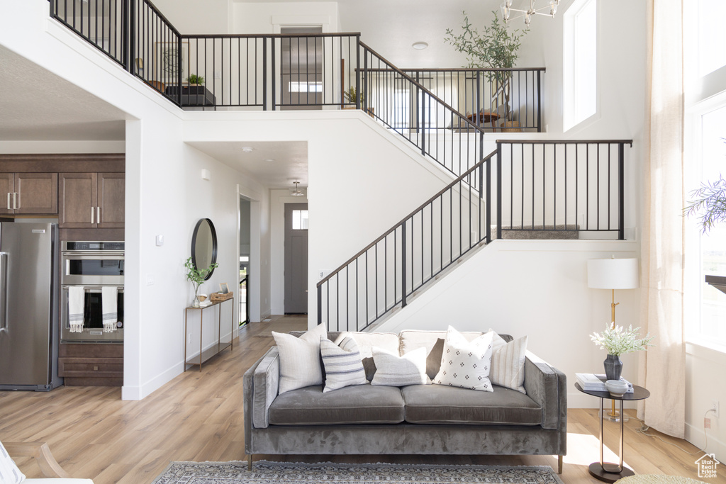 Living room with stairs, light wood-style floors, plenty of natural light, baseboards, and a towering ceiling