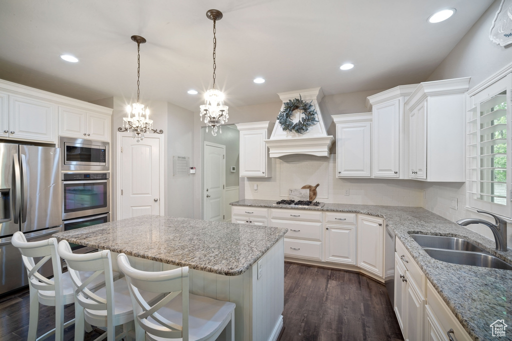 Kitchen featuring stainless steel appliances, a sink, a kitchen island, a chandelier, and light stone countertops