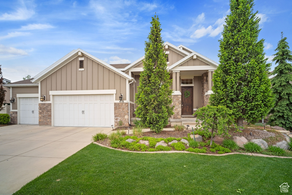 View of front of house featuring board and batten siding, stone siding, an attached garage, driveway, and a front lawn