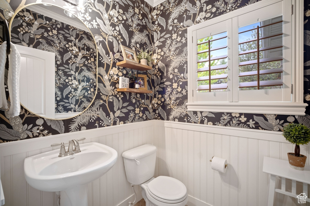 Bathroom with wallpapered walls, a sink, wainscoting, toilet, and ornamental molding