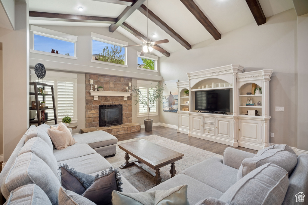 Living area with ceiling fan, wood finished floors, a stone fireplace, beam ceiling, and high vaulted ceiling