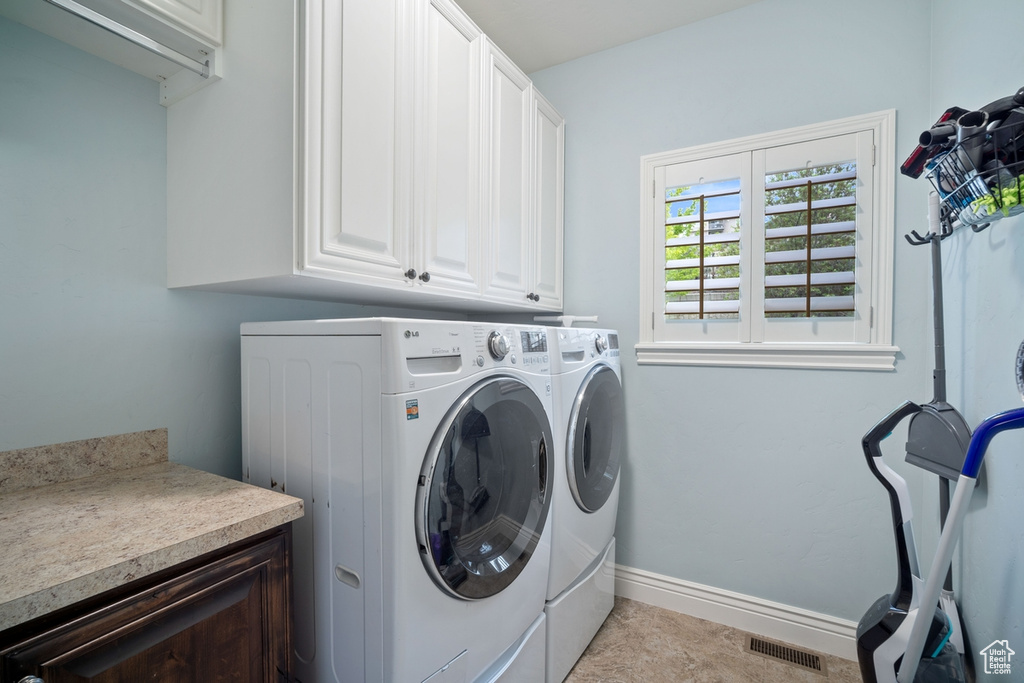 Clothes washing area with cabinet space, washer and dryer, and baseboards
