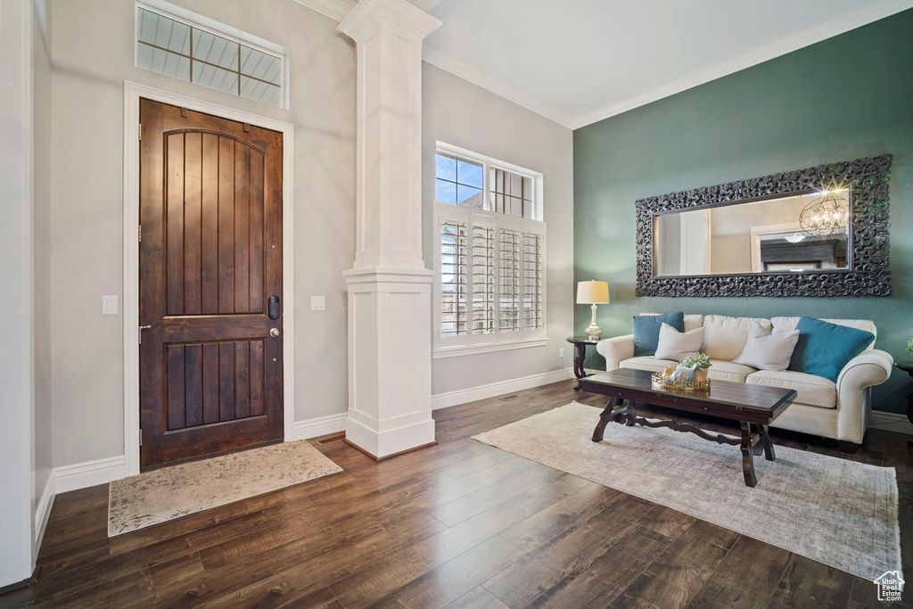 Entryway featuring ornate columns, wood finished floors, baseboards, ornamental molding, and a chandelier