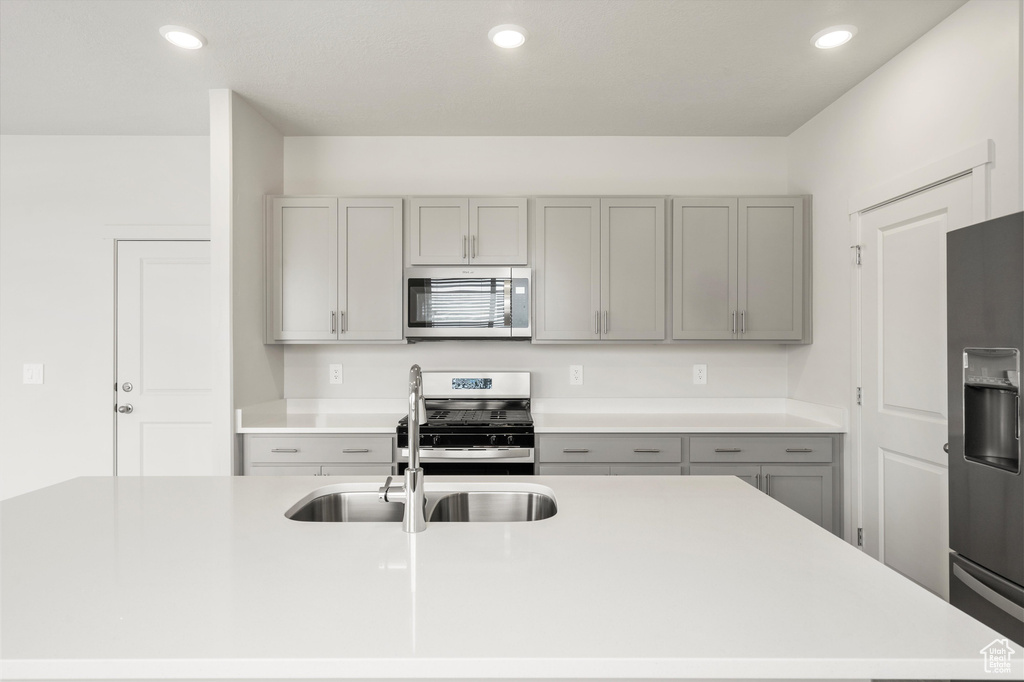 Kitchen featuring appliances with stainless steel finishes, gray cabinets, light countertops, recessed lighting, and a kitchen island with sink