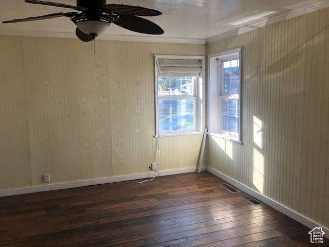 Empty room with dark wood-style flooring, crown molding, a ceiling fan, and baseboards
